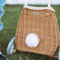 Rattan bunny luggy with a white fluffy tail, floral Gumdrop lining and wheels, shown on grass by Olli Ella Kids Rattan