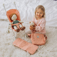 Child playing with a doll in a rose stroller beside a matching quilted stroller seat and bag on a soft white rug from Dinkum Dolls