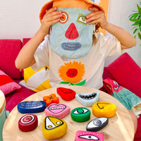 Child playing with colorful Tubbles sensory stones featuring interchangeable facial features, with a character pouch and expression pieces on a table from Olli Ella Kids