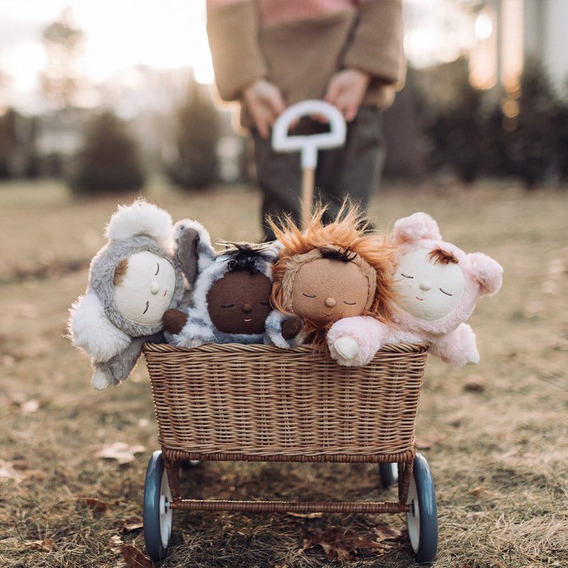 Cozy Dinkums Zebra Mini and three plush dolls nestled in a wicker toy stroller outdoors, ready for imaginative play and cozy adventures.