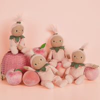 Four peach themed Dinky Dinkums dolls in pink outfits with leafy collars posed among fresh peaches on a soft pink background