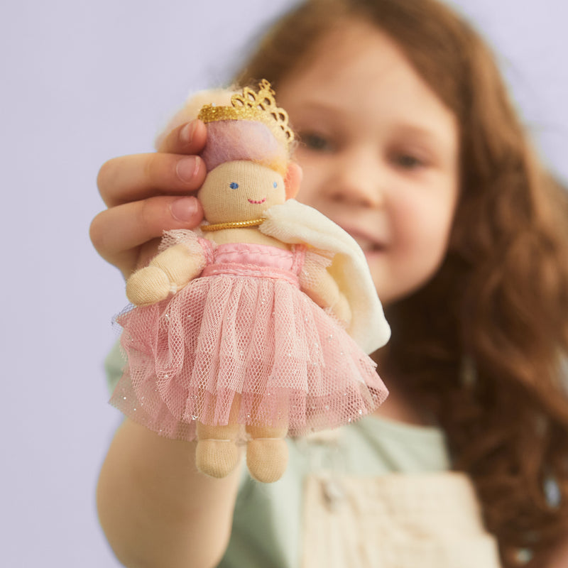 Child holding a poseable Holdie Princess Gloribel doll wearing a pink tutu dress, gold crown, and white cape against a soft lavender background