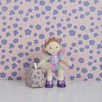 Dinkum Dolls toy doll dressed in a sparkly fairy outfit with purple tutu, wings and boots, standing beside a matching floral suitcase against a flowered backdrop