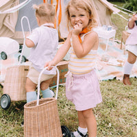 Child pulling a natural rattan Luggy basket on wheels at an outdoor picnic, featuring a woven design and sturdy handle from Olli Ella Kids Rattan